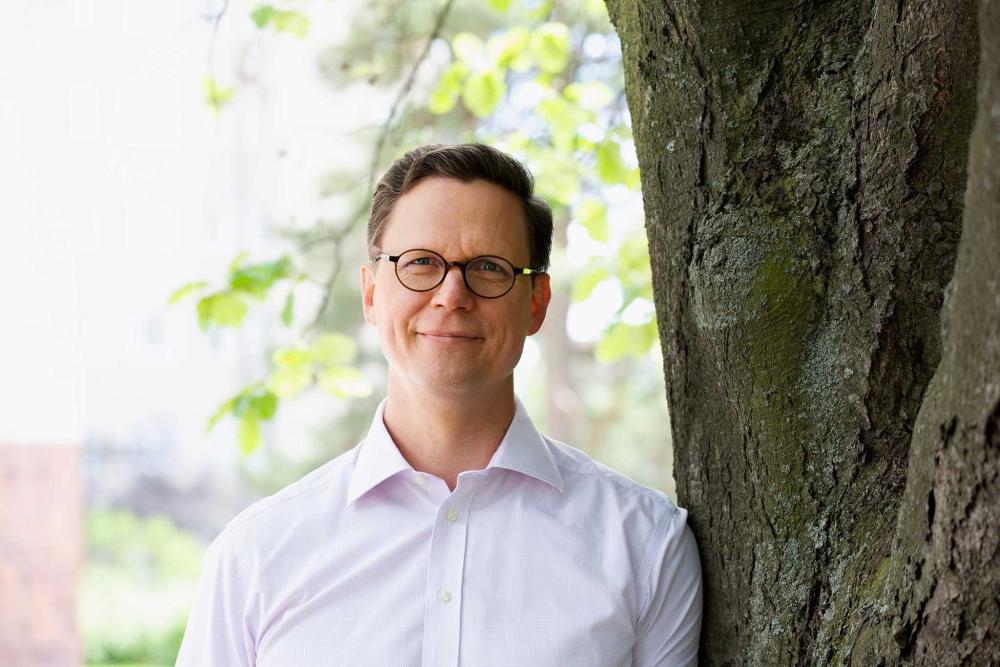 Ombudsman for Equality, Mr. Jukka Maarianvaara stands next to a tree on a sunny day and smiles.