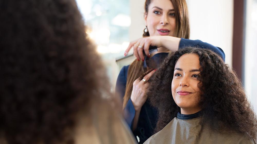 Smiling woman with curly hair being treated by a hairdresser.