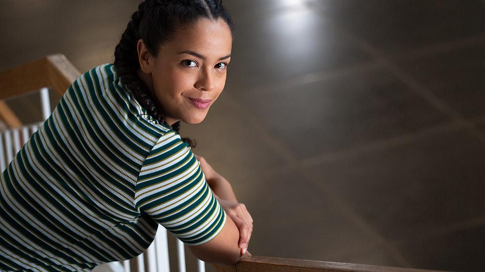 A young woman leans on the stair railing and looks at the camera with a smile.